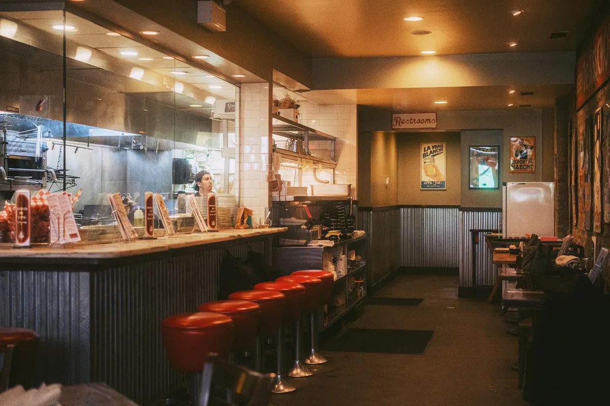 Warm and inviting interior of a classic American diner with red stools and open kitchen.