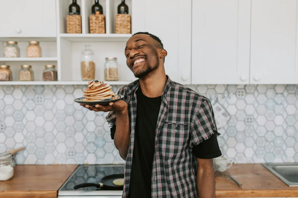 Happy man smiling and holding a plate of pancakes in a stylish kitchen setting.