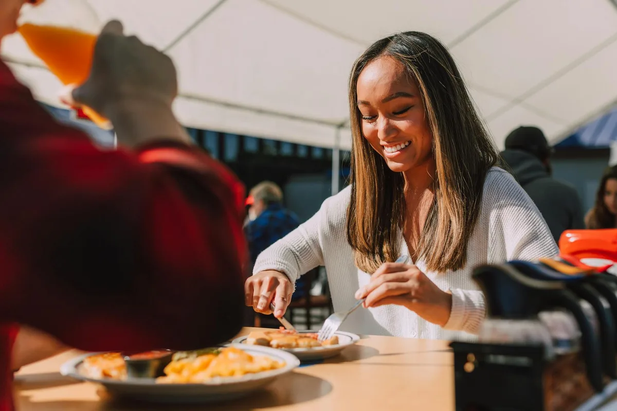 A woman enjoying a meal outdoors, smiling and relaxed at a sunlit table.